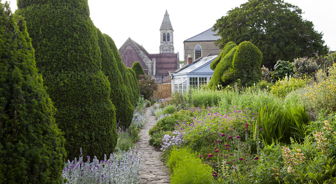 The Yew Walk at The Courts Garden, Wiltshire, in June. The church in view in the distance is not National Trust.